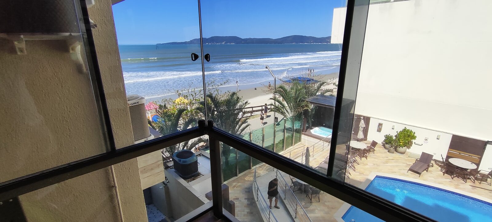 Varanda de canto em vidro, com vista da piscina do condomínio e do mar