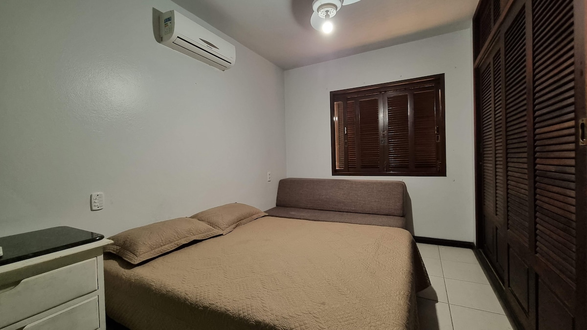 Quarto com cama de casal, cabeceira de madeira e ar-condicionado