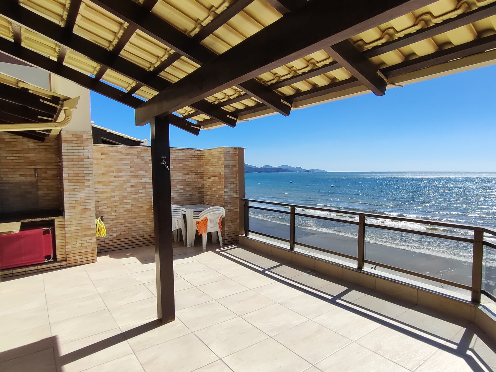 Terraço amplo sob pergolado de madeira com vista panorâmica do mar