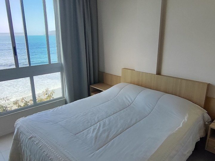 Suíte com cama de casal, luminária e vista mar