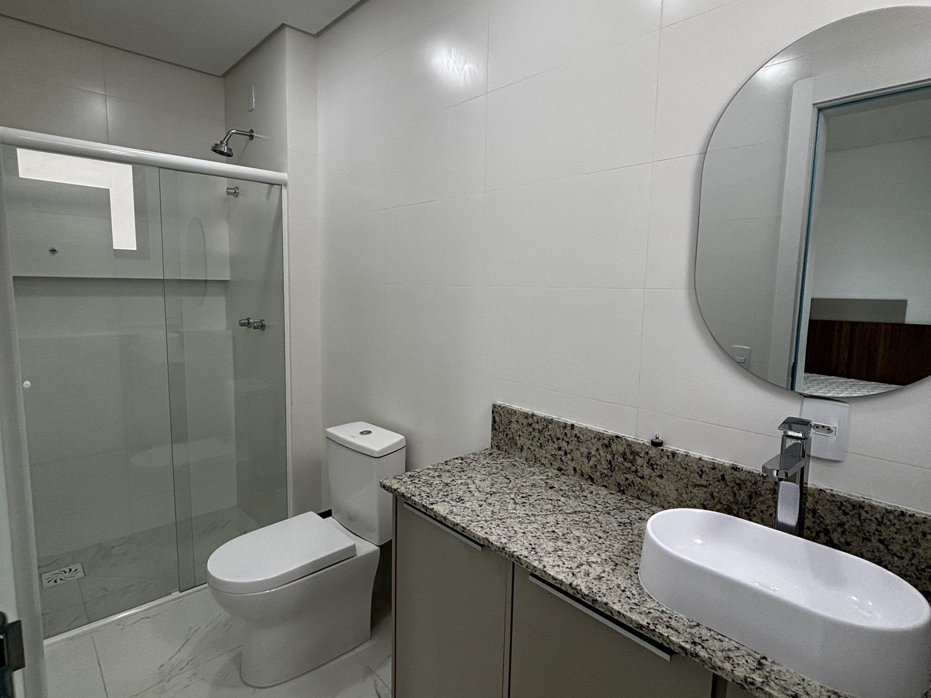Banheiro de suíte com box de vidro e bancada de granito