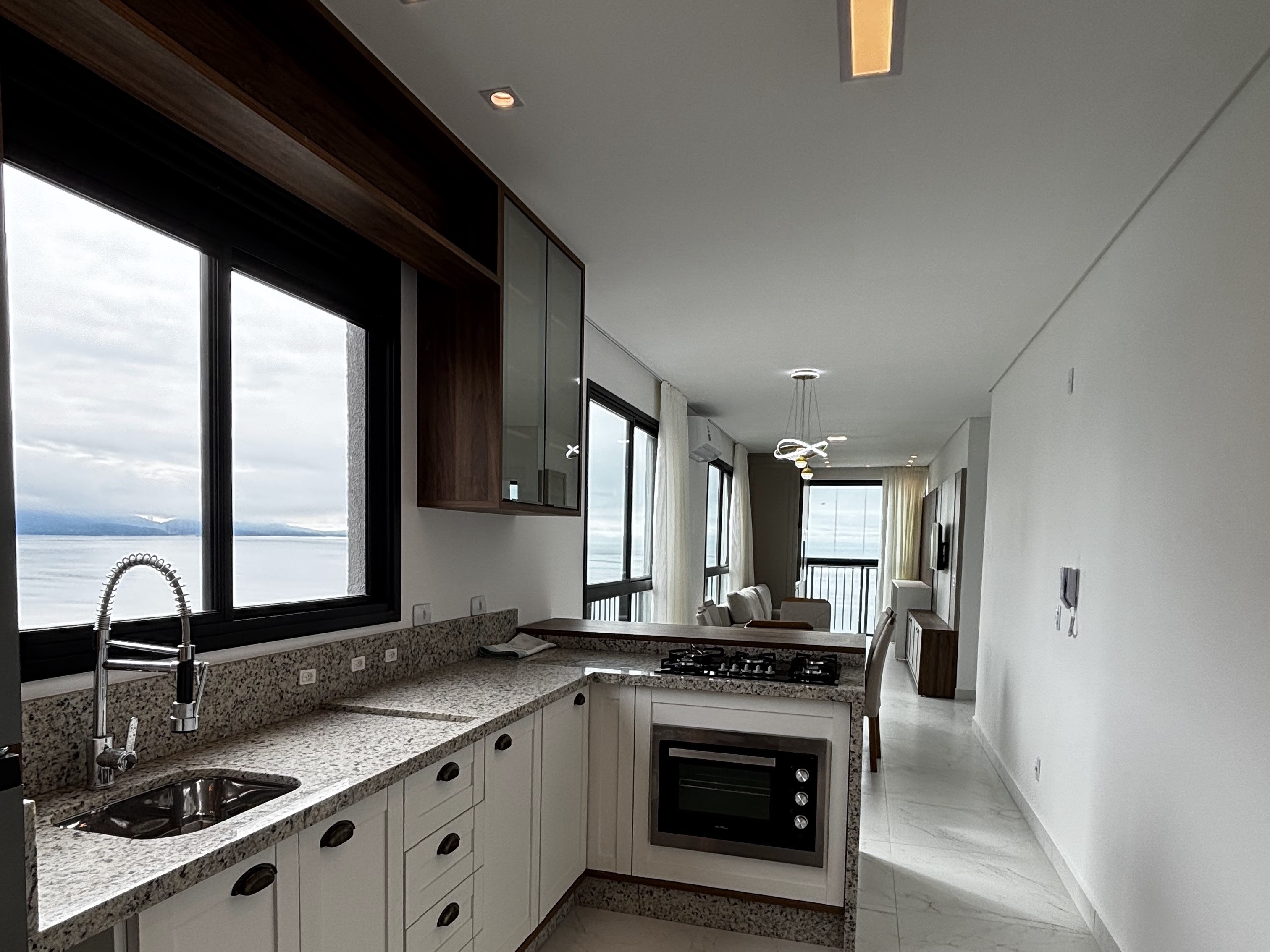Cozinha americana com armários, bancada de granito, cooktop a gás e vista para o mar