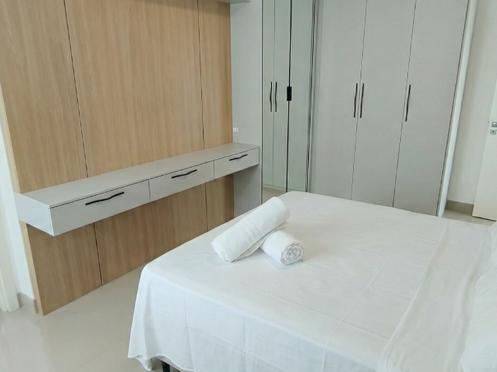 Suíte com cama de casal e marcenaria em madeira clara