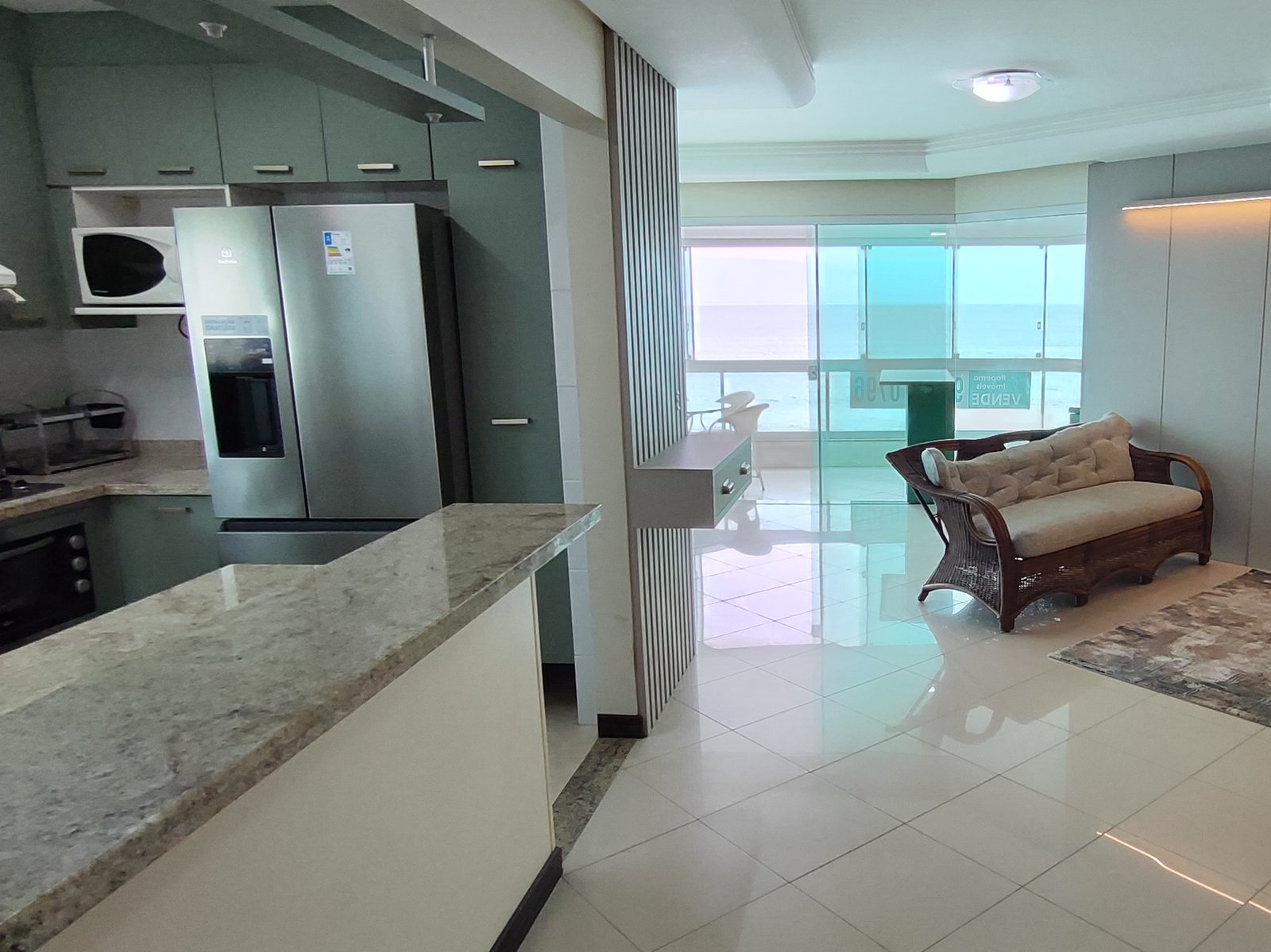 Cozinha equipada com geladeira inox e vista para a sala de vidro