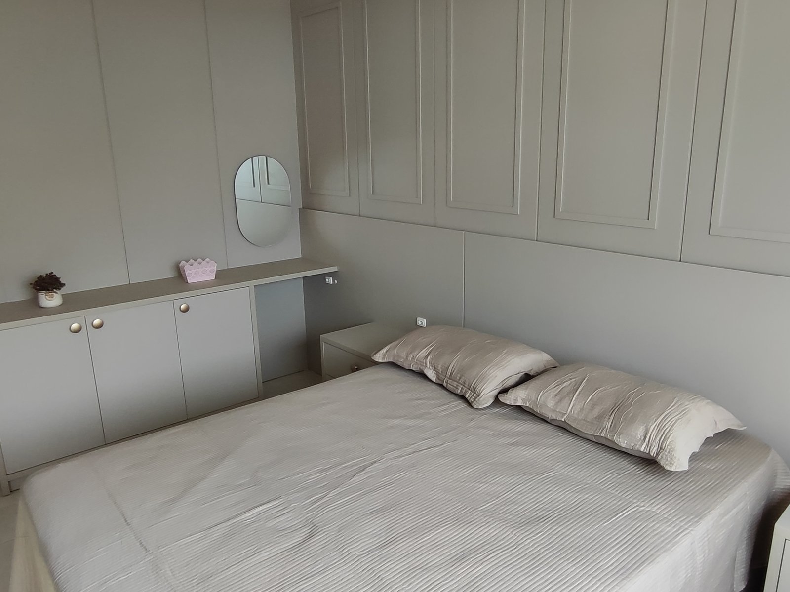 Quarto com cama de casal e espelho oval sobre a cômoda