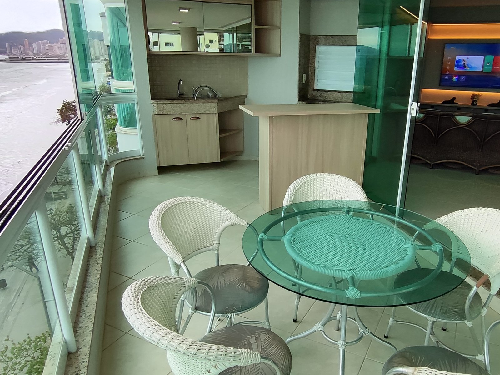Mesa bistrô redonda na sala de vidro, com vista para o mar e acesso à cozinha