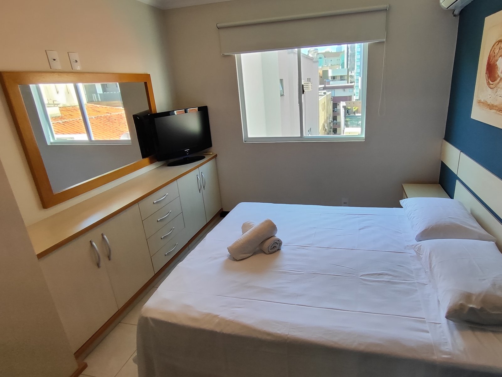 Quarto com cama de casal e móvel com espelho e TV