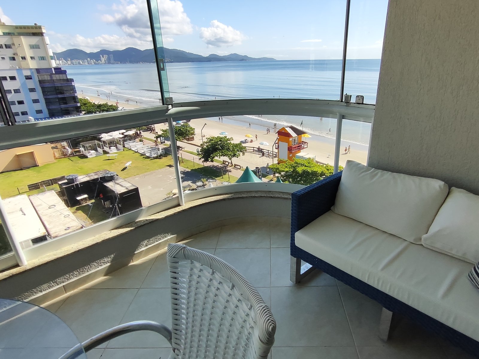 Sala de estar integrada à varanda de vidro, com vista para o mar