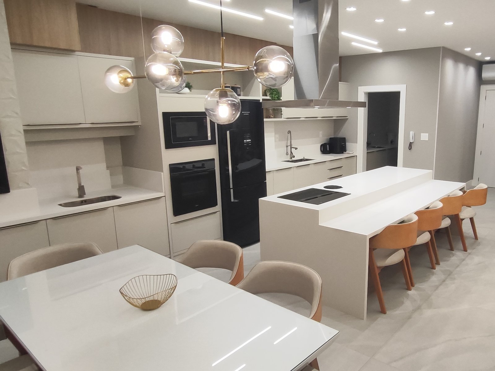 Cozinha integrada com ilha, cooktop, adega e lustre dourado