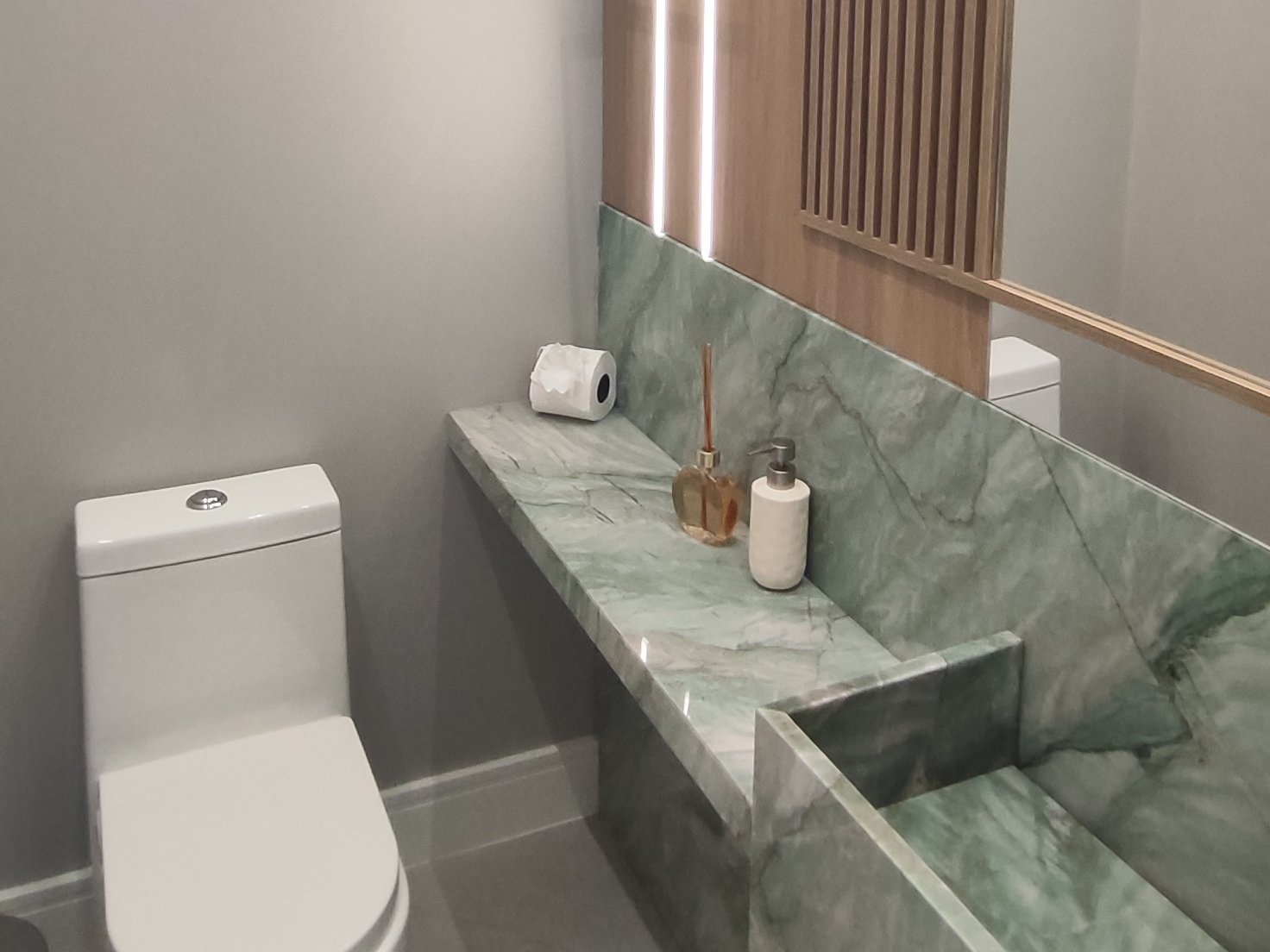 Lavabo com bancada em mármore verde e painel de madeira ripada