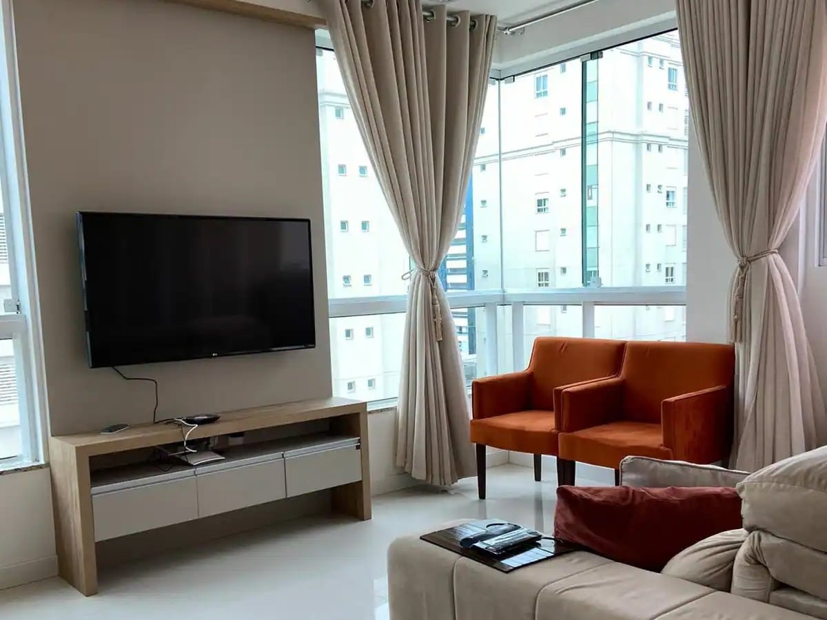Sala de estar com sofá, poltronas laranja e Smart TV