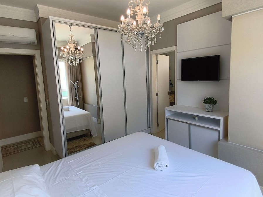 Suíte com cama de casal, closet espelhado e lustre de cristal