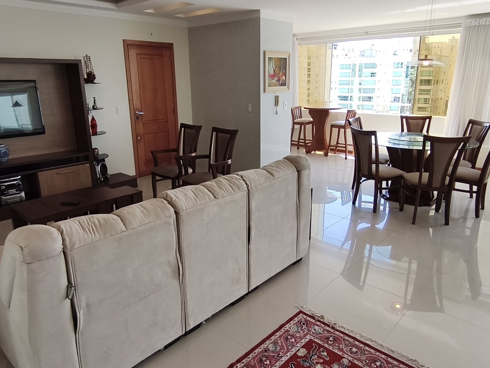 Sala de estar com sofá amplo, TV e jantar ao fundo