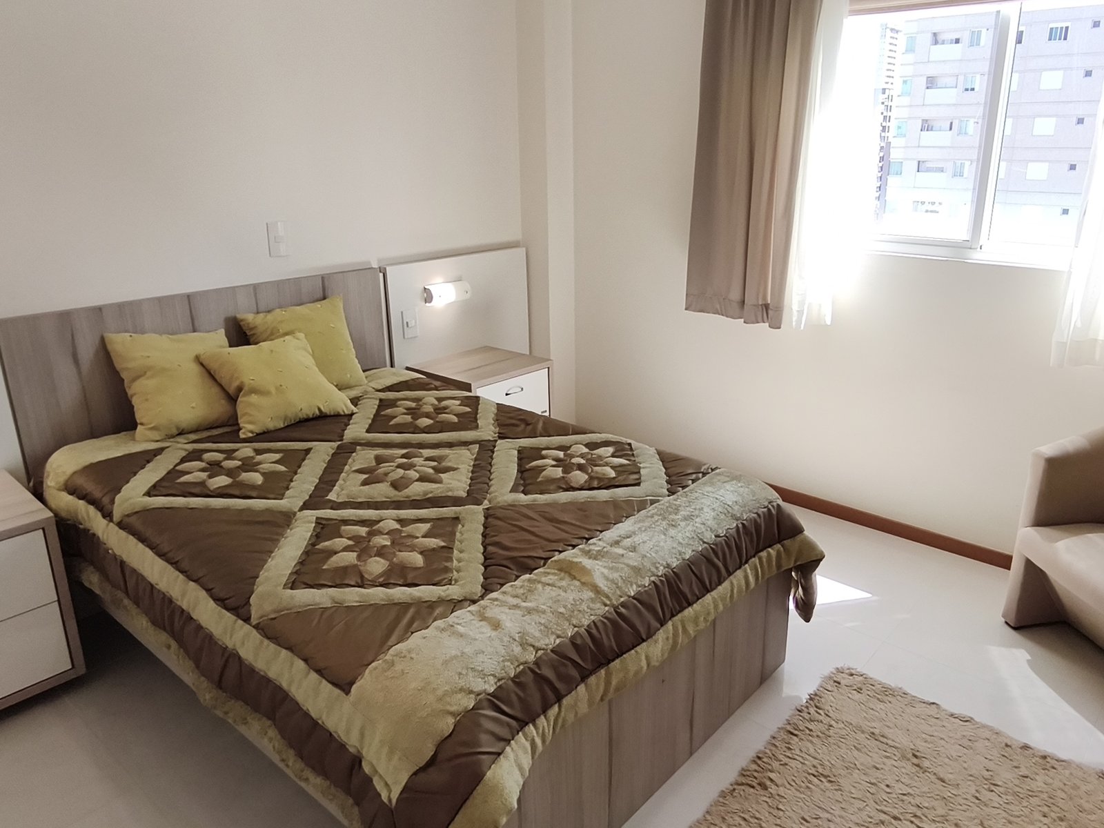 Suíte com cama de casal, colcha dourada e poltrona