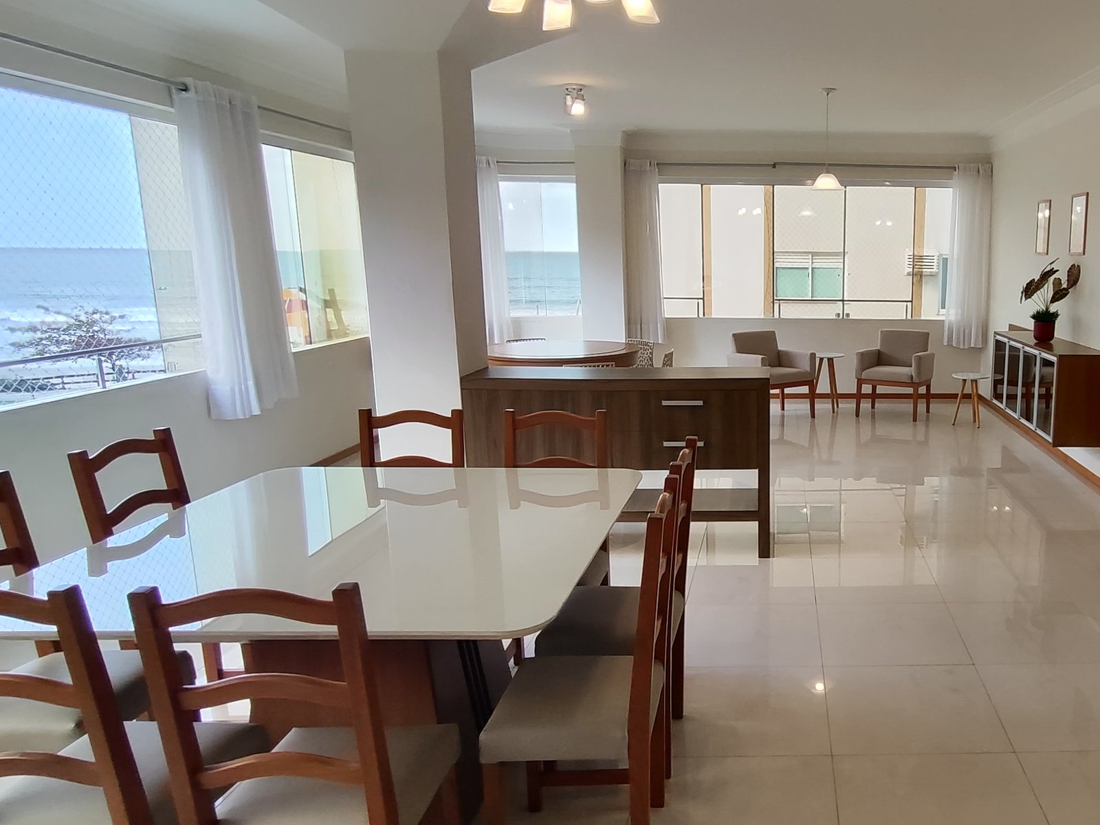 Sala de jantar integrada à sala de estar, com janelas de frente pro mar
