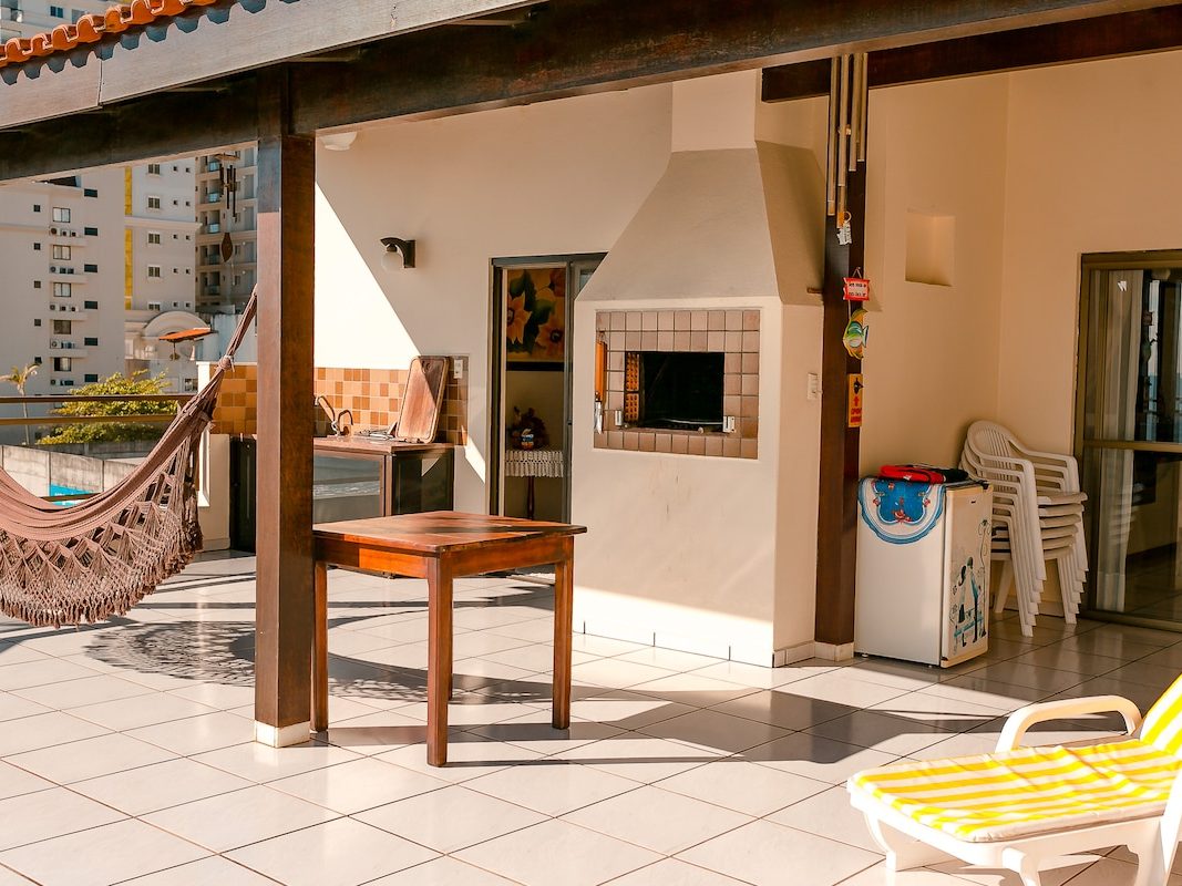 Área gourmet coberta do terraço, com churrasqueira a carvão, mesa de madeira e rede