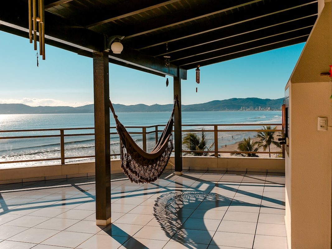 Trecho coberto do terraço, com rede armada e a praia de Meia Praia aberta na frente