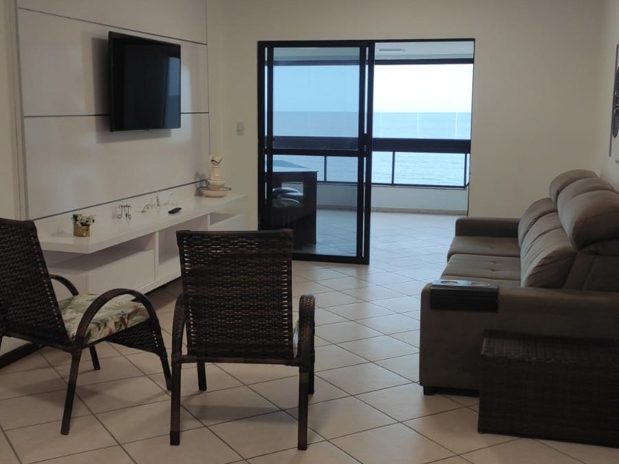 Sala de estar com sofá, TV em painel e porta de vidro para a sacada