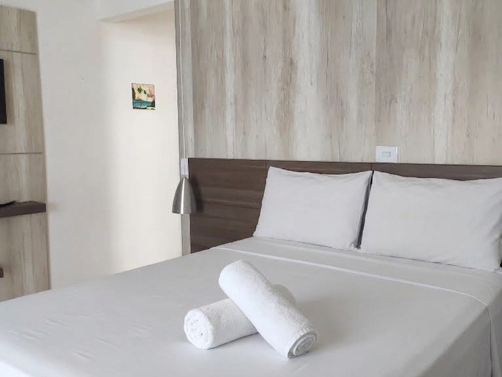 Suíte com cama de casal, painel de madeira e TV própria