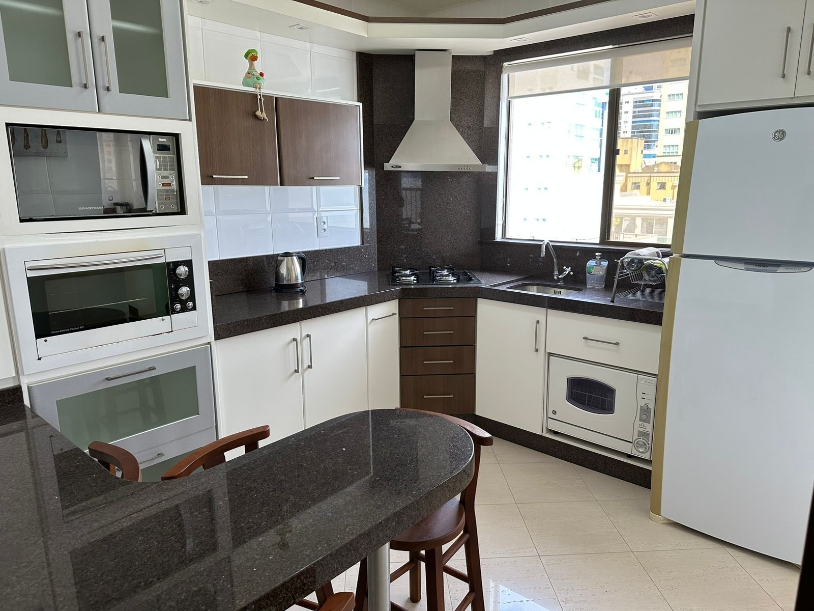 Cozinha completa com cooktop, forno, geladeira e balcão com banquetas