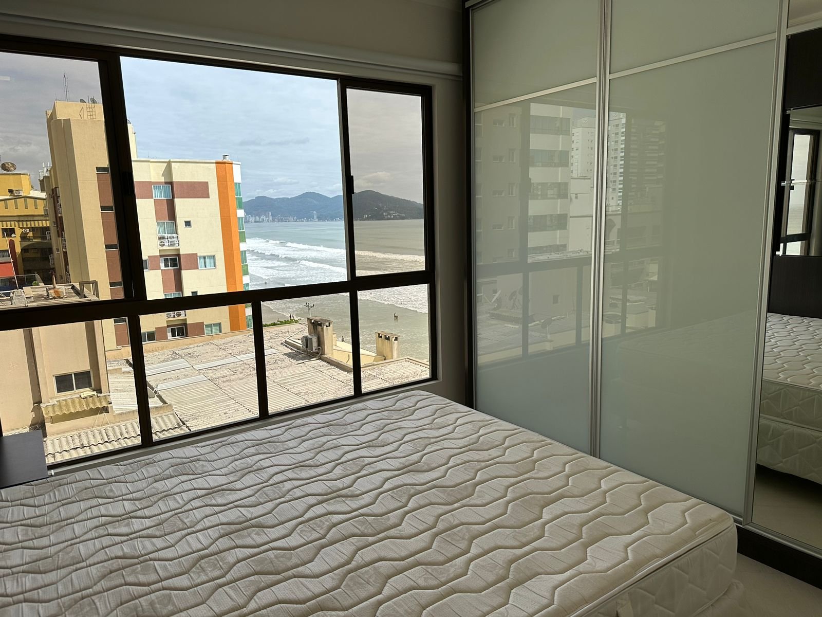 Suíte com cama de casal e porta de vidro para a varanda, vista mar direto do quarto