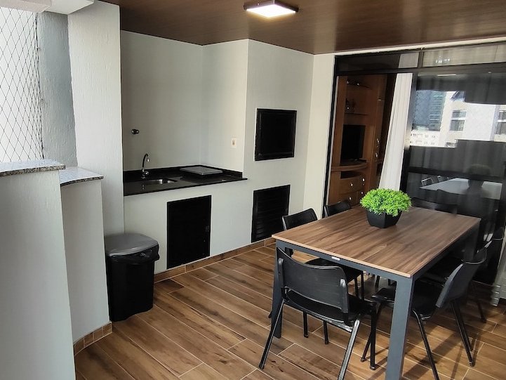 Varanda gourmet com pia, TV e mesa de jantar externa